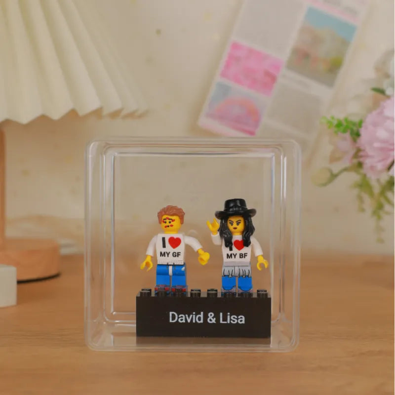 Two LEGO figures in a clear display case with 'I ❤️ MY GF' and 'I ❤️ MY BF' text, on a wooden surface.