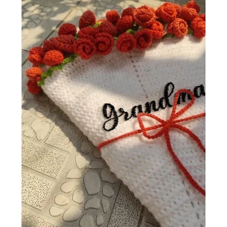 White blanket with red floral trim and 'Grandma' embroidery on a textured surface