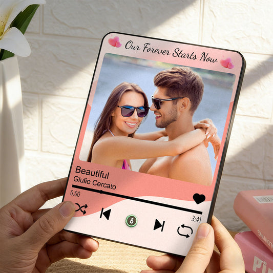 Phone displaying a romantic photo of a couple with music player interface, held by hands against a light background.