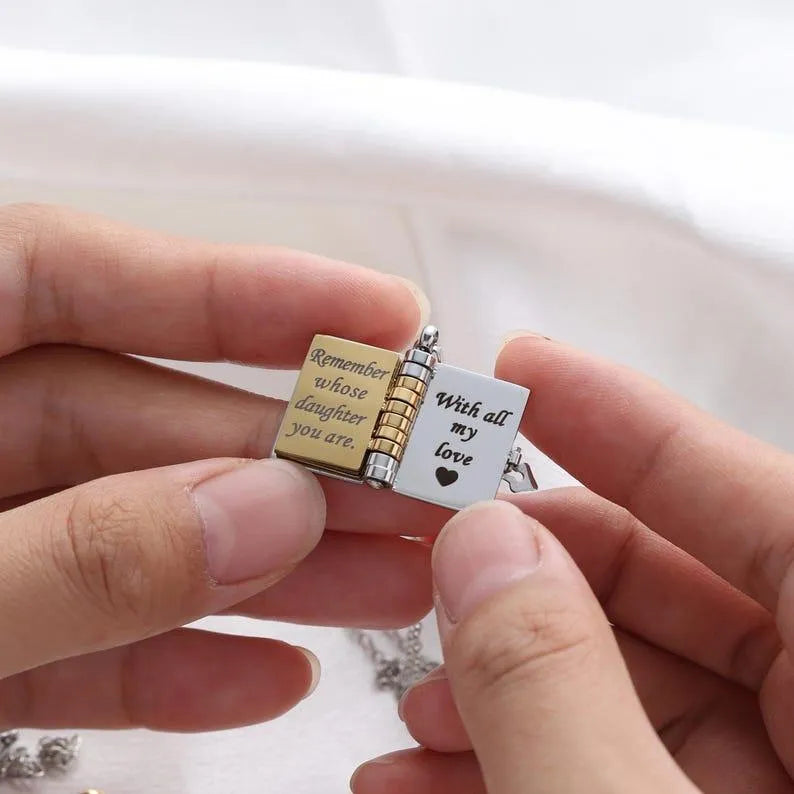 Two small charms held by a hand, one with text and a heart, the other with a book design.