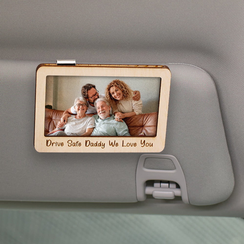 Wooden photo frame with family picture and engraved text on a car's sun visor.