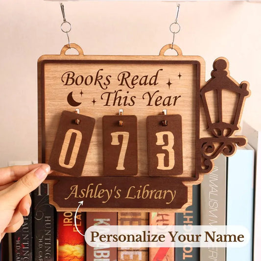 Wooden plaque with 'Books Read This Year' and decorative elements, held over books.
