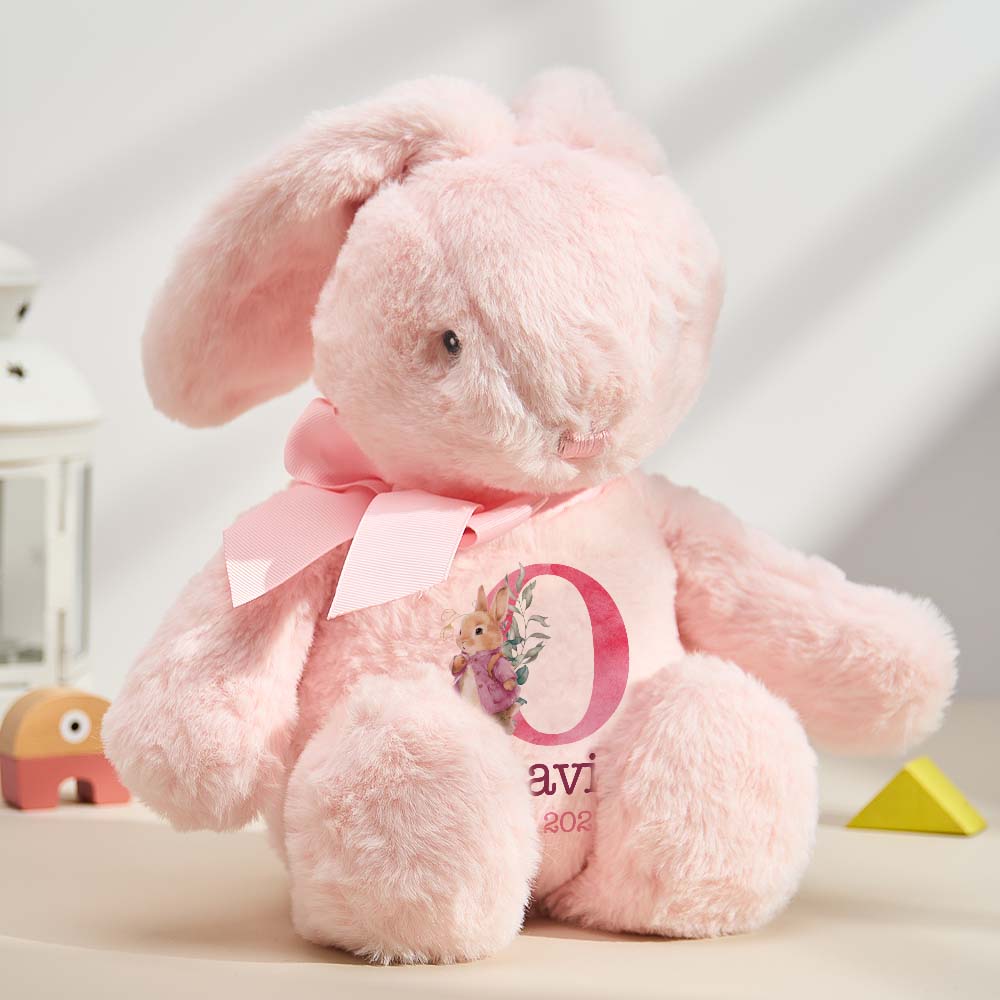 Pink plush bunny with a bow and letter 'O' on a light background