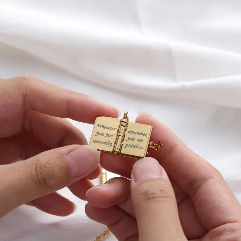 Gold pocket book charm held between two hands with a white background
