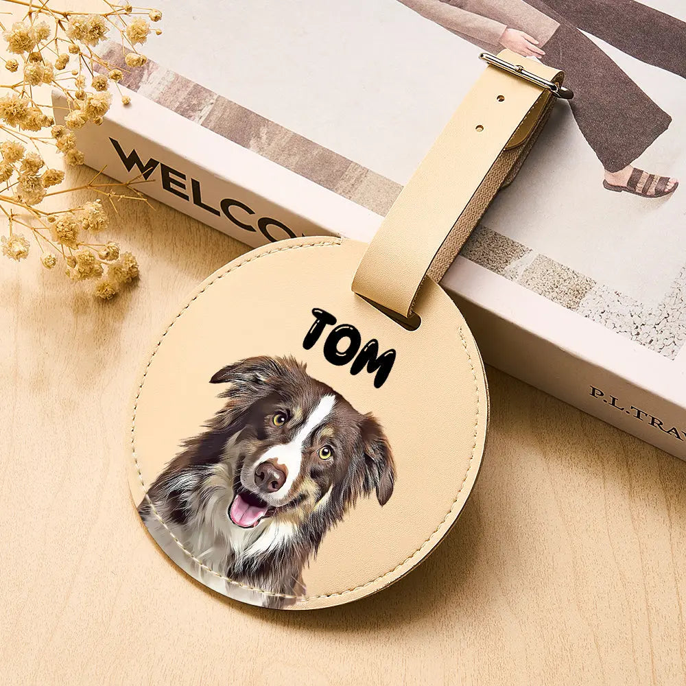 Round leather tag with a dog's face and name 'Tom' on a wooden surface with books and flowers.