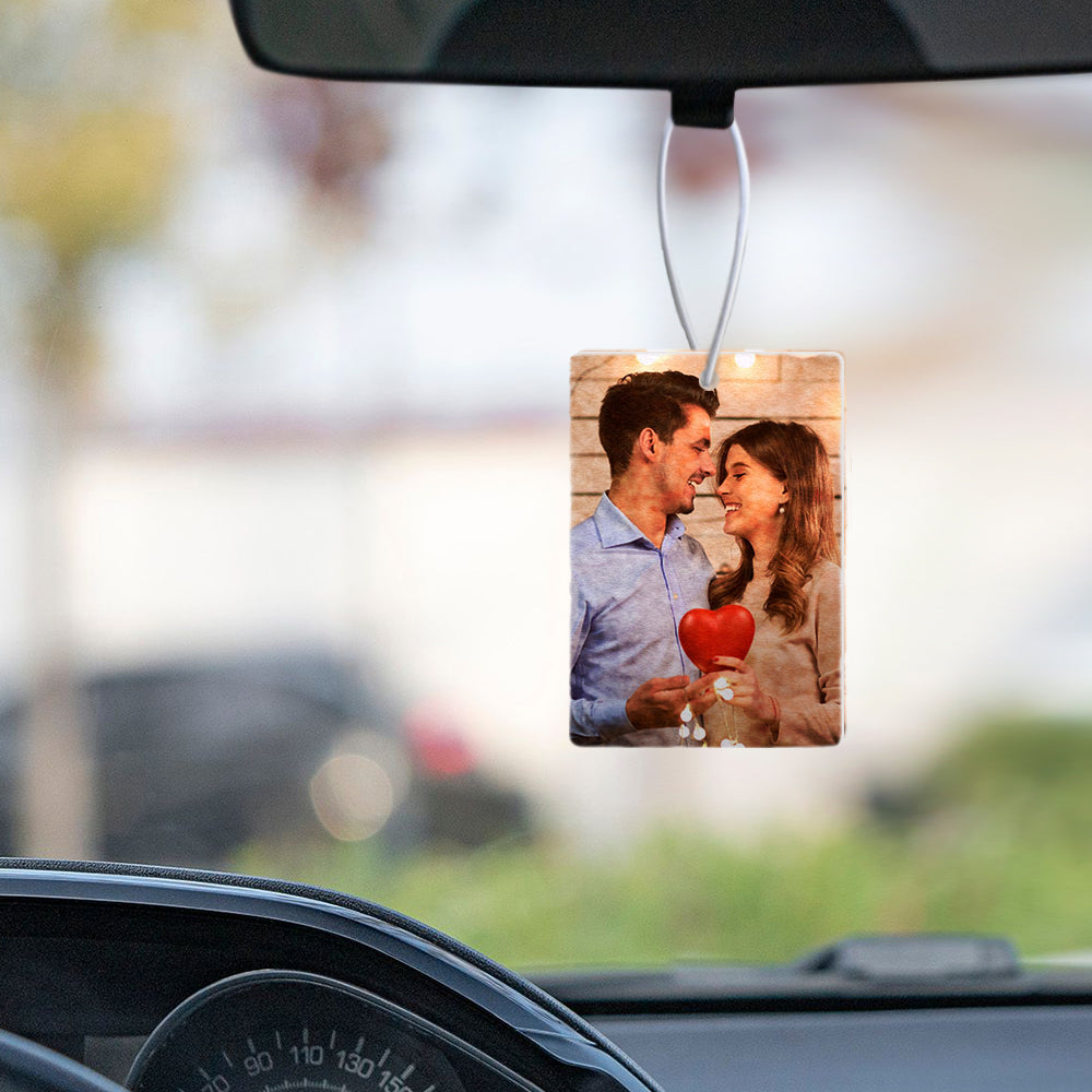 Car air freshener with a photo of a couple holding a heart-shaped object hanging from a car's rearview mirror.