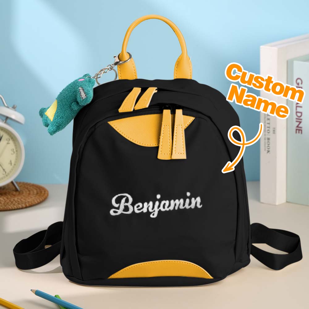 Black backpack with yellow accents and 'Benjamin' embroidered on it, placed on a surface with a light blue background.