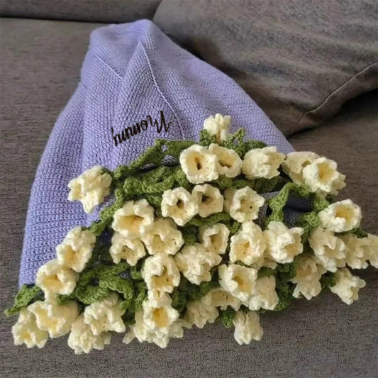 Knitted bouquet of flowers on a textured surface with a blanket and pillow in the background.