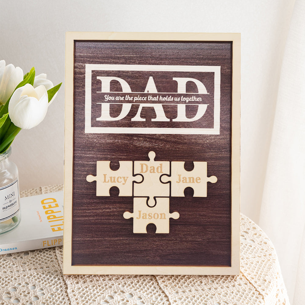 Wooden plaque with puzzle pieces for 'DAD' and names on a textured surface with flowers.
