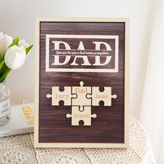 Wooden plaque with puzzle pieces for 'DAD' and names on a textured surface with flowers.