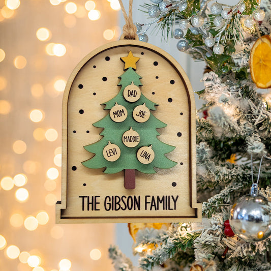 Wooden Christmas tree ornament with family names on a decorated tree with lights.