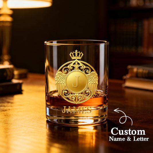 Glass with gold emblem and 'JAMES' engraving on a wooden surface.