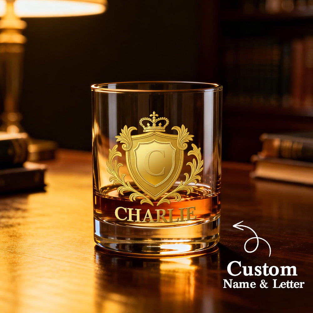 Glass with gold emblem and 'CHARLIE' engraving on a wooden surface, blurred background