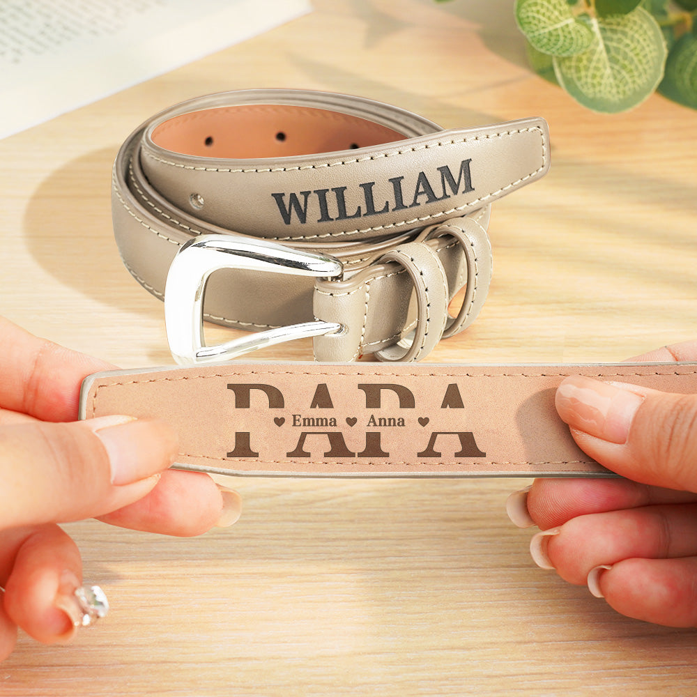 Two leather belts with engraved text held by hands on a wooden surface.