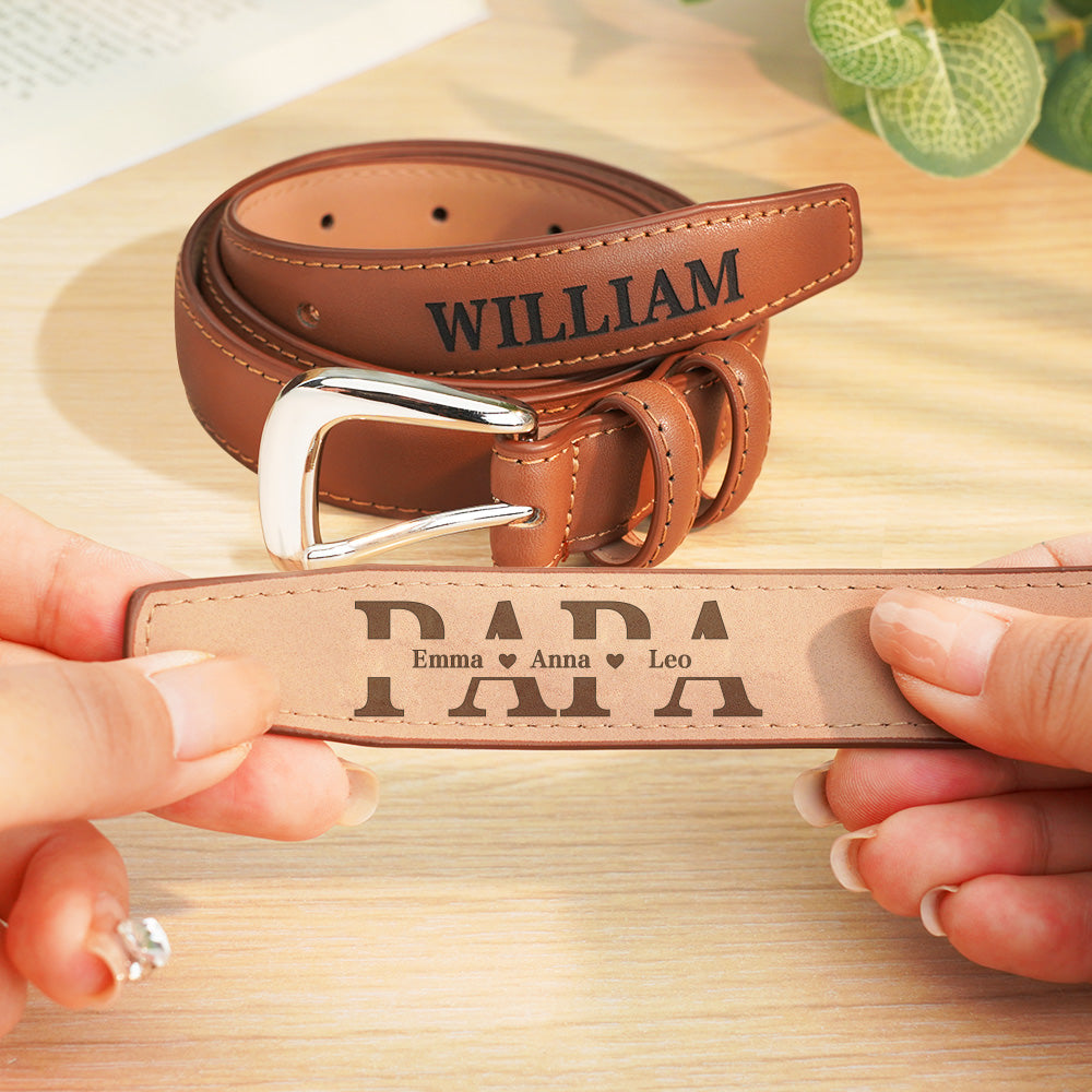 Brown leather belt with 'WILLIAM' engraved, held by hands on a wooden surface.