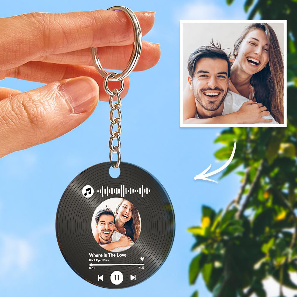 Keychain with vinyl record design featuring a couple's photo and music notes, held by a hand with a blue sky and green leaves in the background.