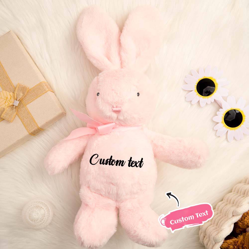 Pink plush bunny with customizable text on a soft surface with flowers and a gift box.