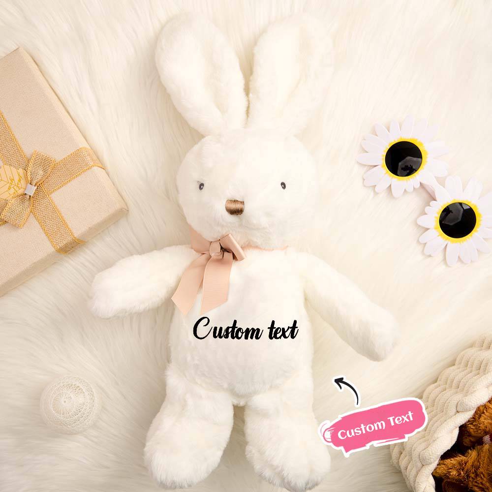 White plush bunny with a pink bow, gift box, and flowers on a soft surface