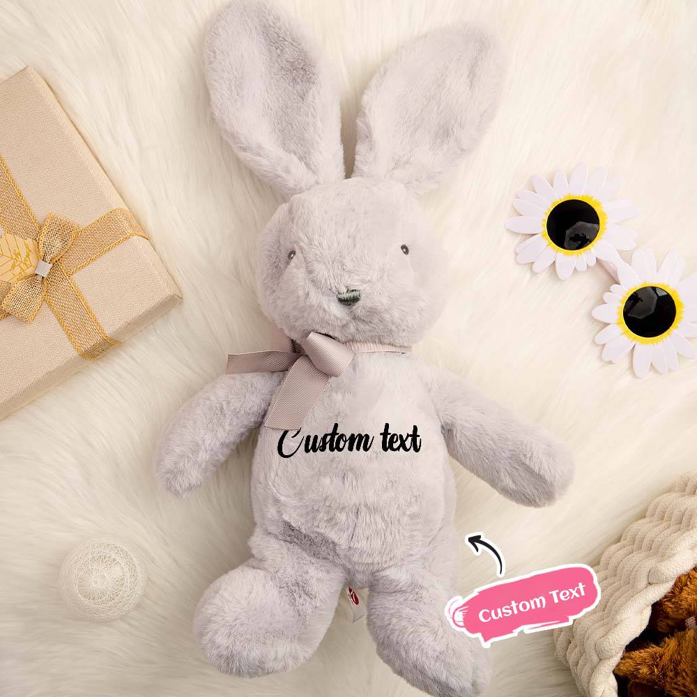 Gray plush bunny with customizable text on a soft surface with flowers and a gift box.