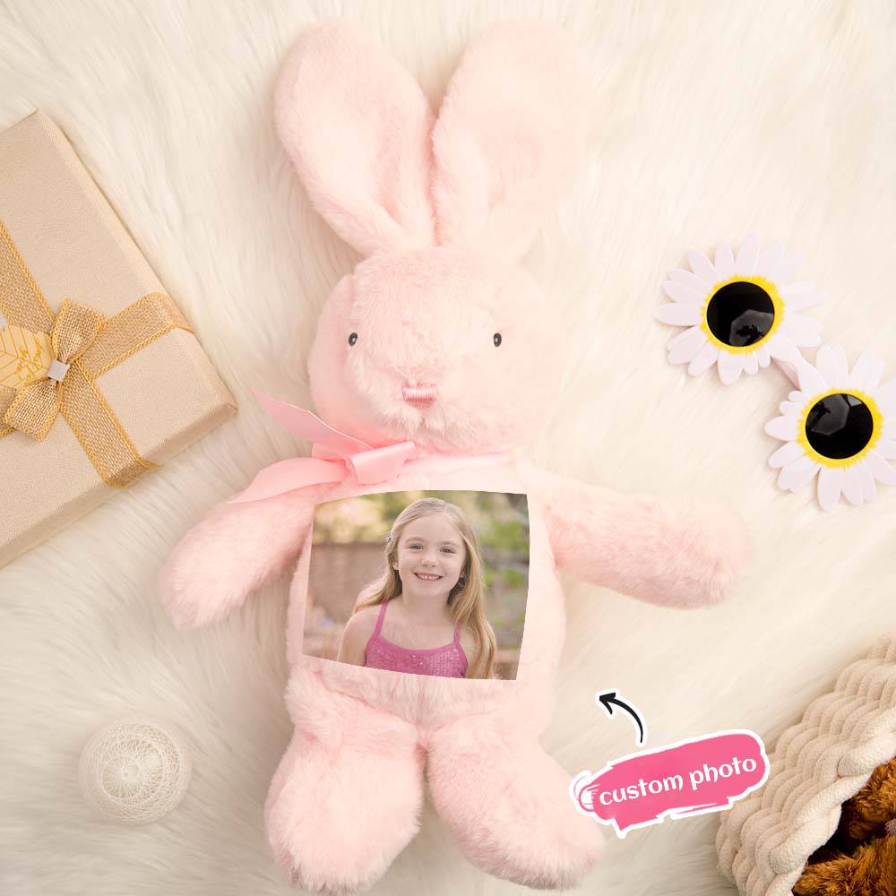 Pink plush bunny with a custom photo display on a soft surface with a gift and flowers.