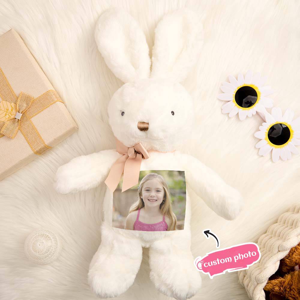 White plush bunny with a photo frame, gift box, and flowers on a soft surface