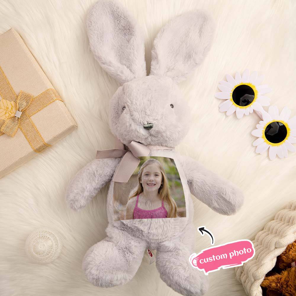 Gray stuffed bunny with a custom photo inside, surrounded by decorative elements on a soft surface.