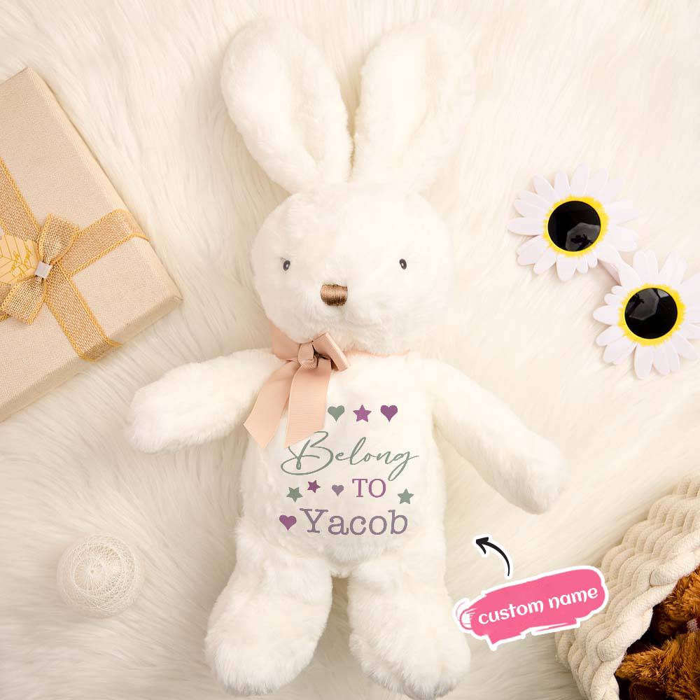 White teddy bear with 'Belong TO Yacob' text and customizable name on a soft surface with flowers and gift box.