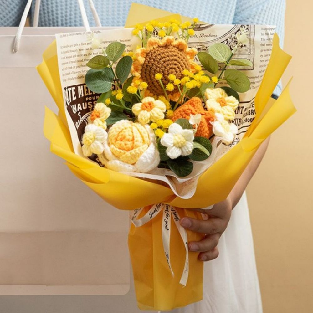 Bouquet of knitted flowers in yellow, orange, and white with a newspaper wrap, held by a person.