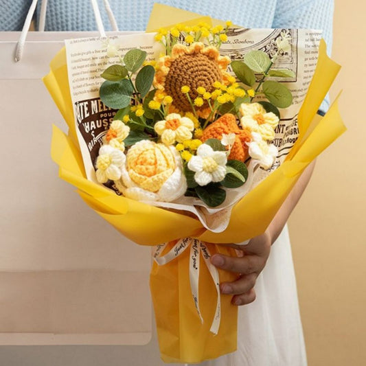 Bouquet of knitted flowers in yellow, orange, and white with a newspaper wrap, held by a person.