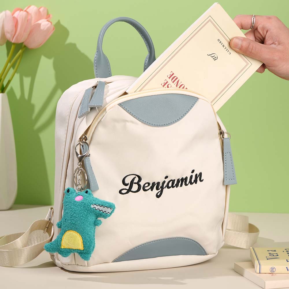Backpack with 'Benjamin' embroidery, shark charm, and hand holding a book against a green background