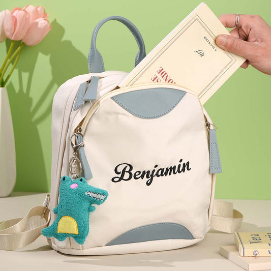 Backpack with 'Benjamin' embroidery, shark charm, and hand holding a book against a green background