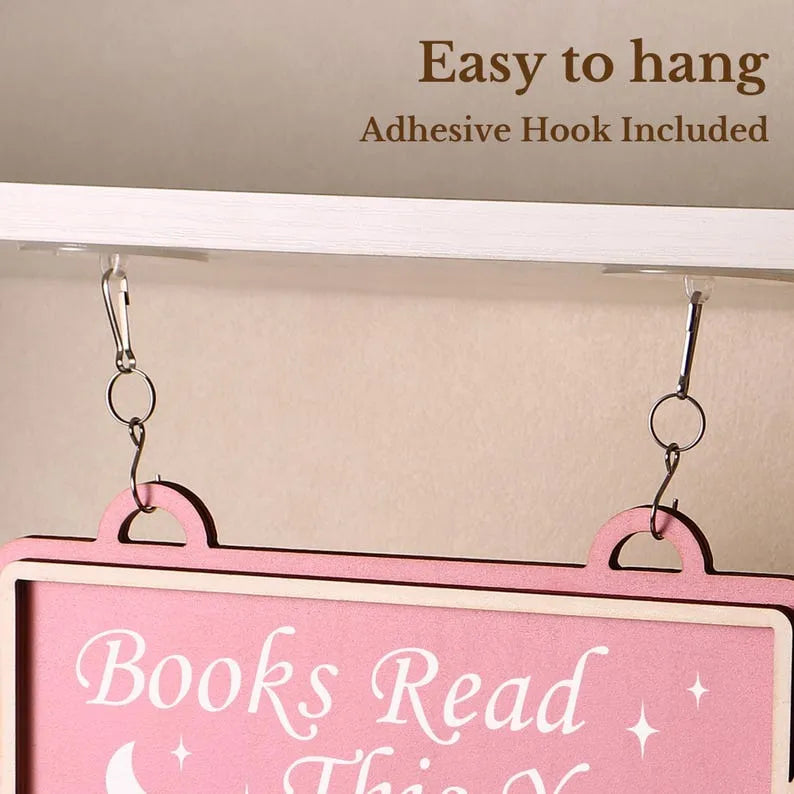Pink sign with 'Books Read' text hanging on a white surface with adhesive hooks.