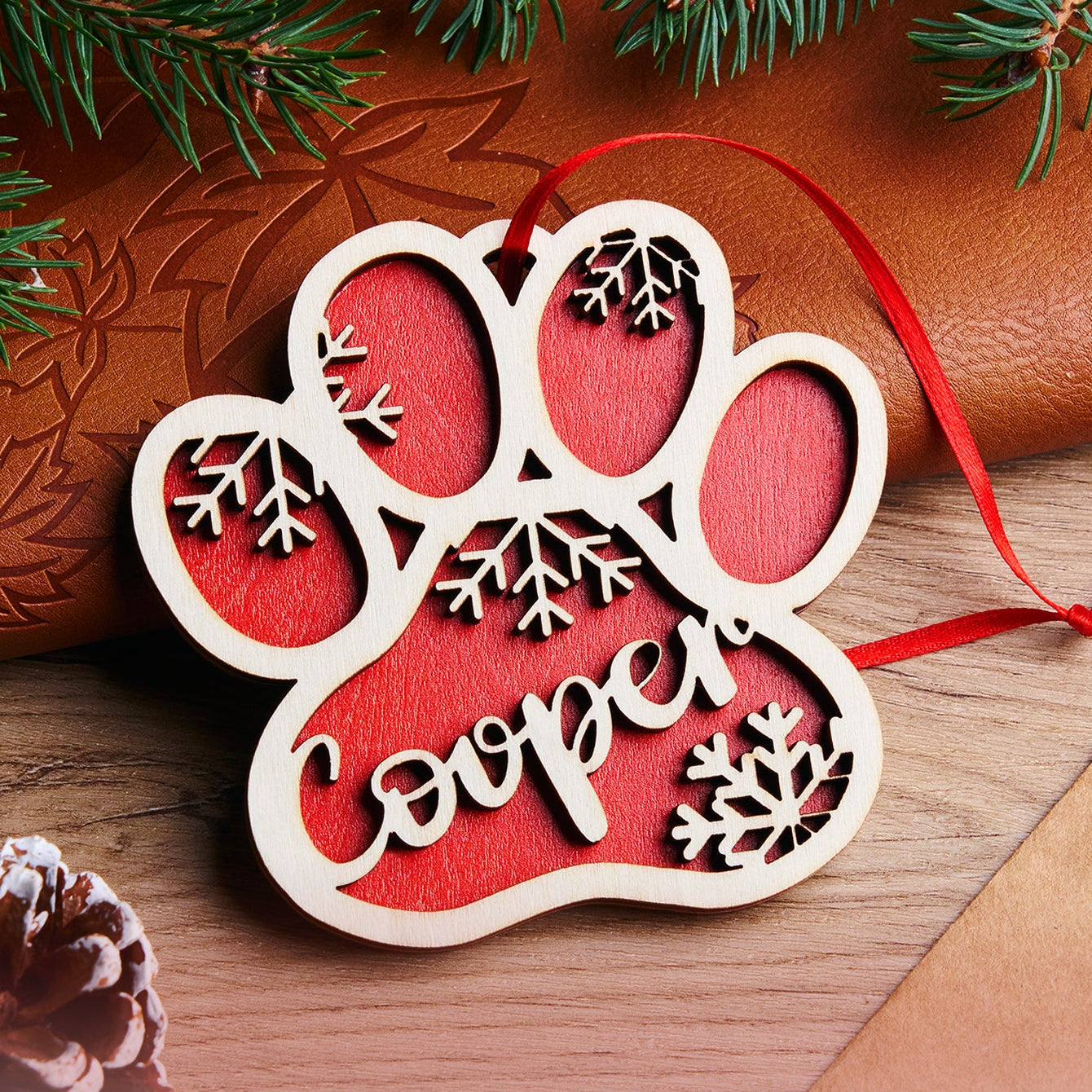 Decorative paw print ornament with 'Cooper' on a wooden surface with Christmas decorations.