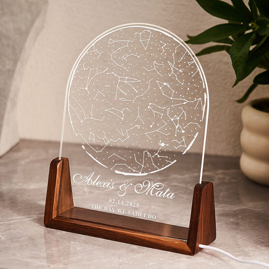 Decorative lamp with engraved constellation design on a wooden base, placed on a surface with a plant in the background.