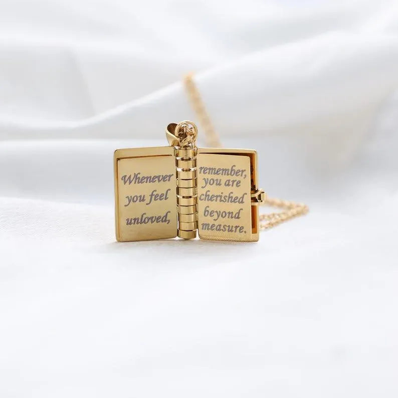 Gold necklace with an open book pendant on a white background